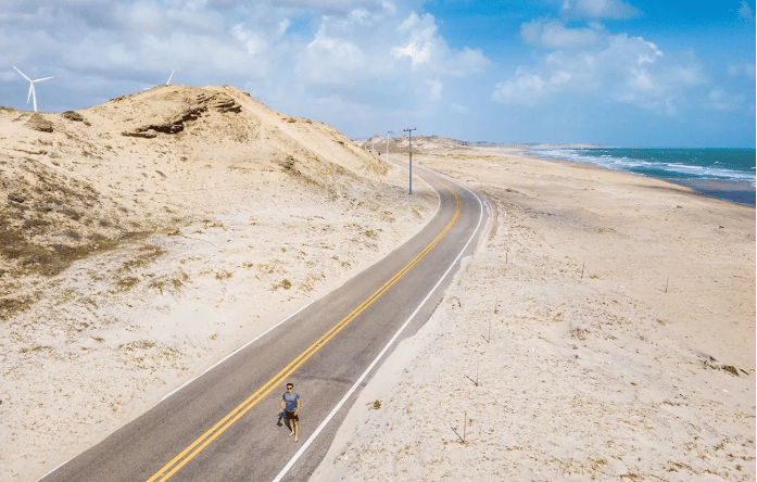 Vista aérea da estrada que corta as dunas em direção à praia de Mundaú, com turbinas de vento ao fundo